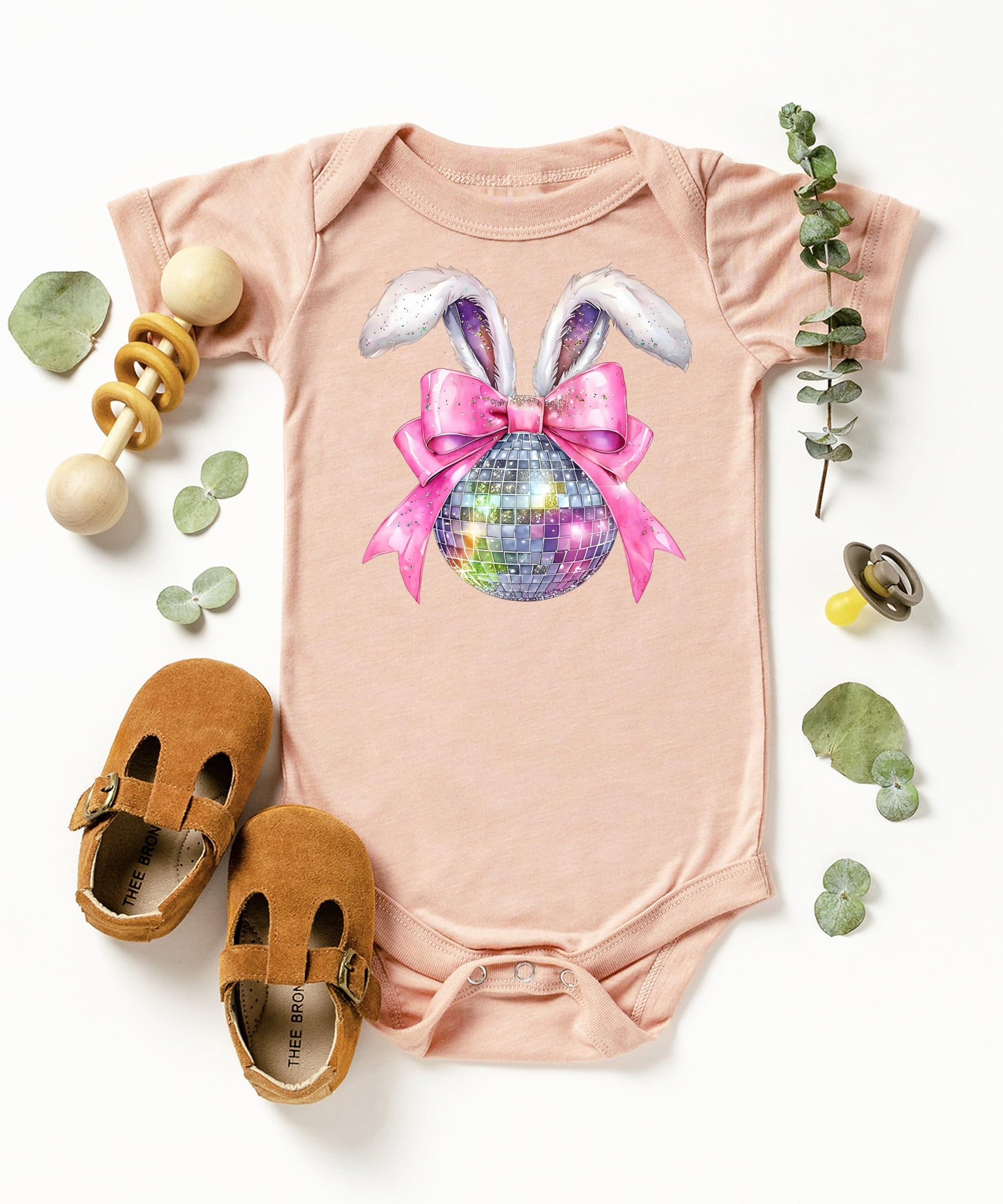Flat lay of peach baby bodysuit with Easter disco bunny graphic — bunny ears and pink bow spring design