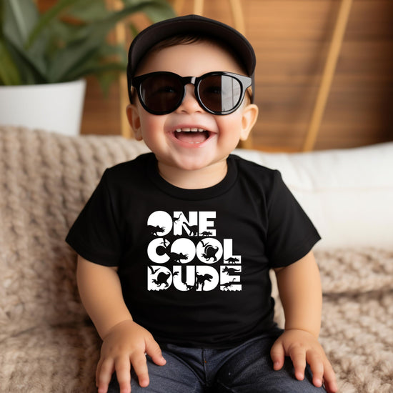 One Cool Dude 1st birthday dinosaur shirt laid flat in military green