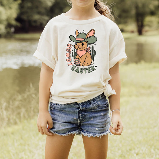 Flat lay of peach youth Howdy Easter western shirt with cowboy bunny, cactus, and Easter egg artwork