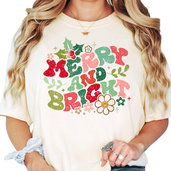 Close-up of distressed Merry and Bright Christmas graphic print with floral details on ivory tee