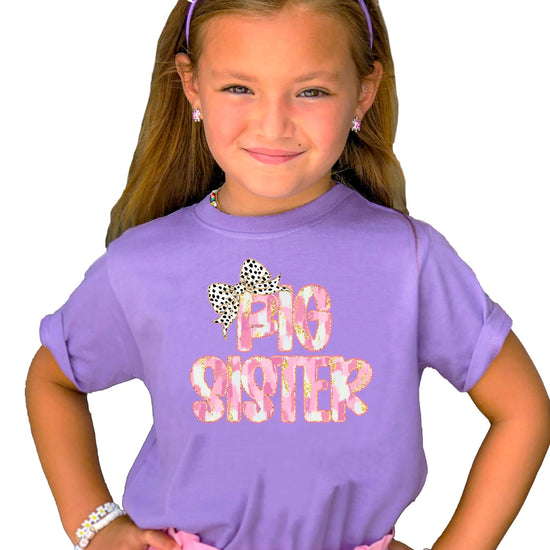 Young girl wearing black Big Sister graphic tee with trendy leopard bow