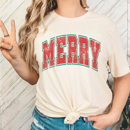 Flat lay of natural Christmas shirt featuring festive varsity letters Merry graphic