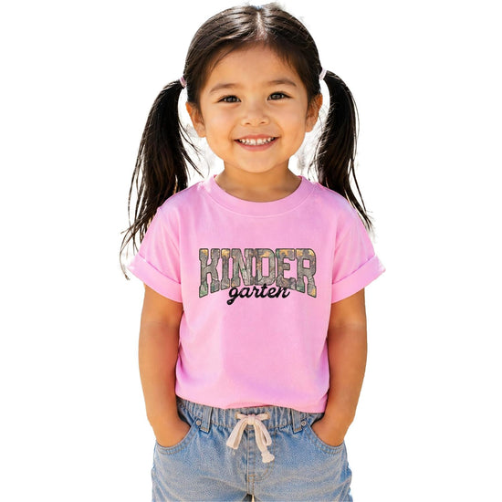 Flat lay of all three colors of the camo Kindergarten shirt — natural, pink, and military green