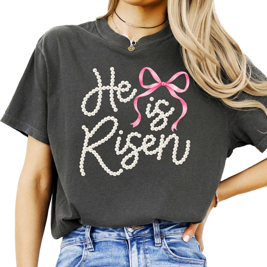 Flat lay of He Is Risen women's Christian t-shirt with coquette bow and resurrection message