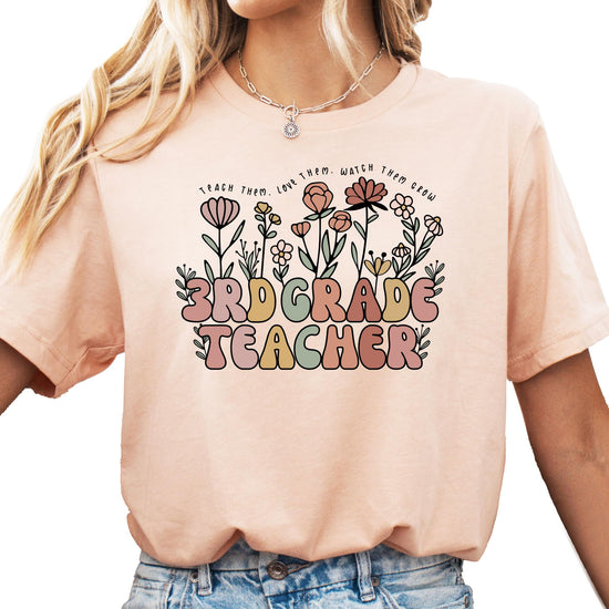 Close-up of floral graphic on women's educator tee with cursive Teach Them Love Them Watch Them Grow text