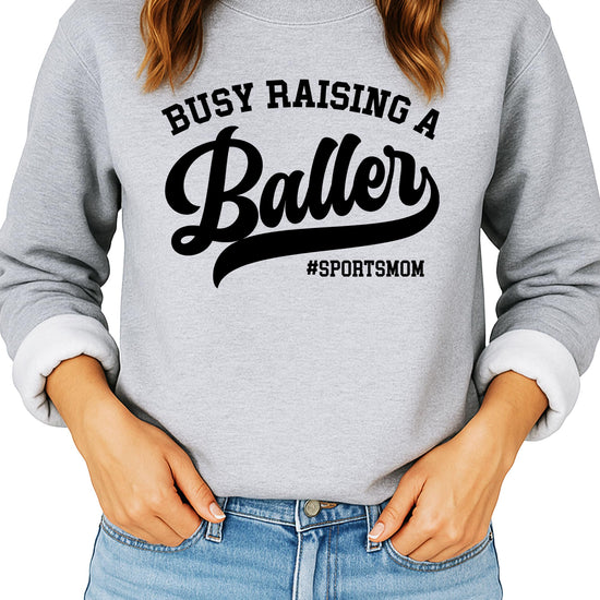 Women's black sweatshirt with 'Busy Raising a Baller' graphic print — sports mom sweater by Olive Loves Apple
