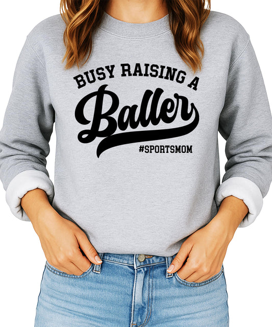 Women's black sweatshirt with 'Busy Raising a Baller' graphic print — sports mom sweater by Olive Loves Apple