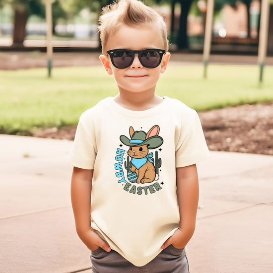 Flat lay of natural youth tee featuring western cowboy Easter bunny and decorated egg graphic
