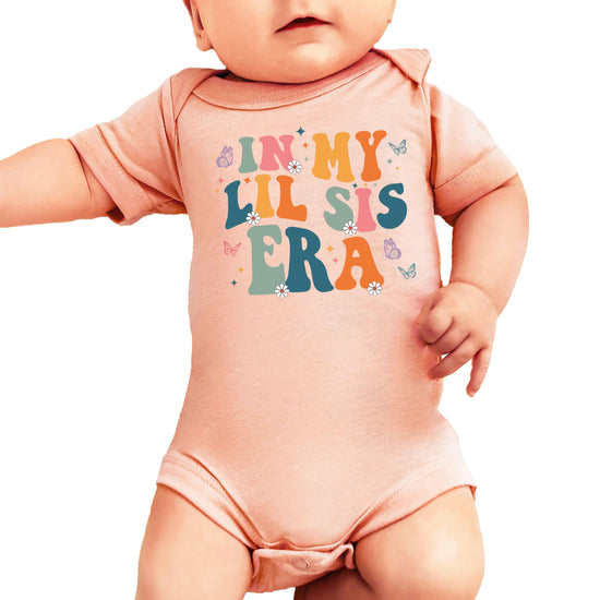 Front view of baby girl one-piece bodysuit with lil sis era graphic in soft peach and floral print