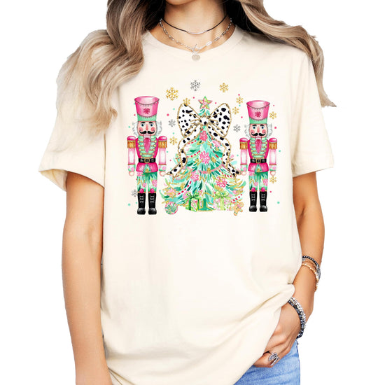 Flat lay of peach women's Christmas shirt with nutcracker and tree design by Olive Loves Apple
