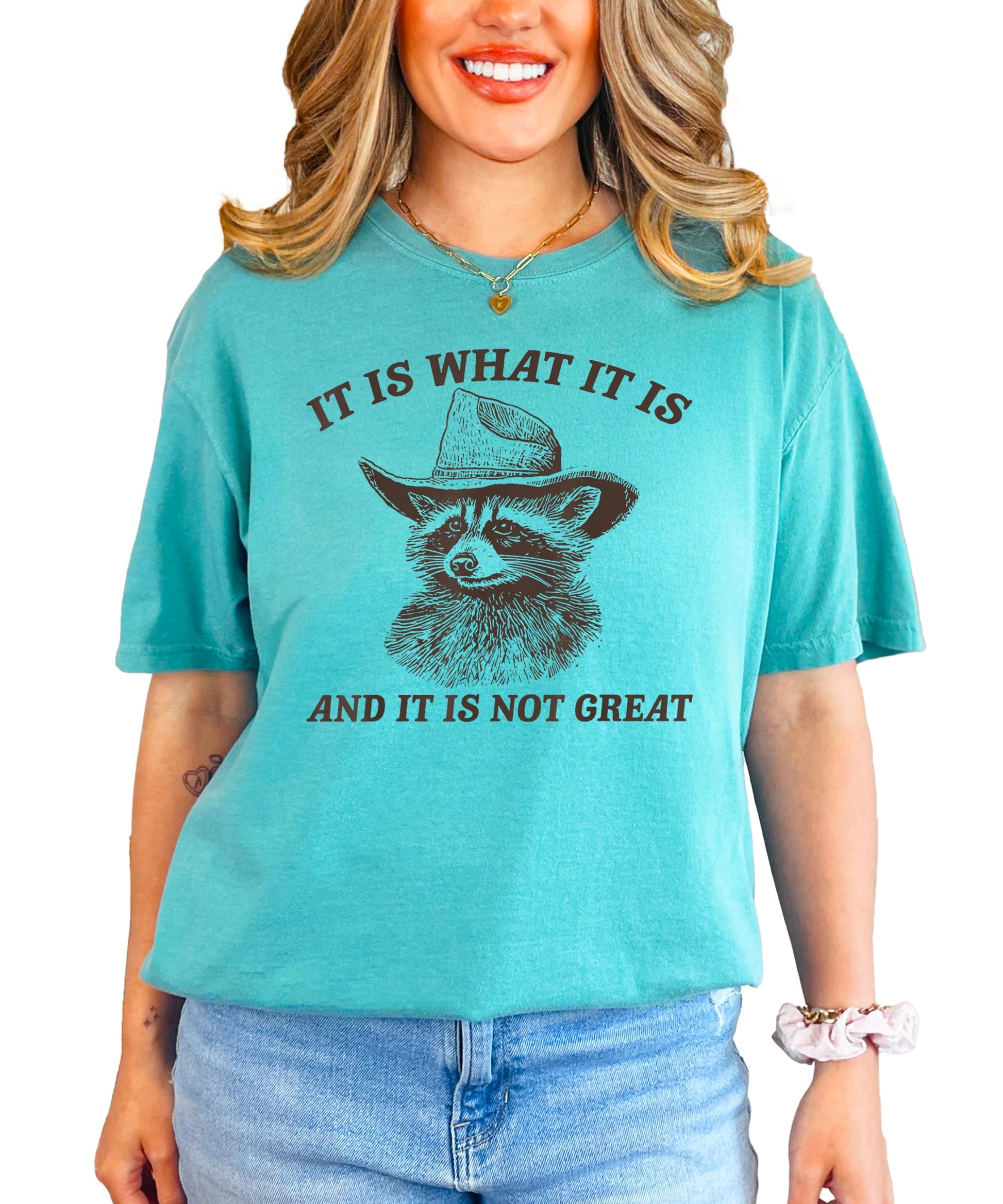 Front view of the It Is What It Is funny raccoon tee in ivory on a female model