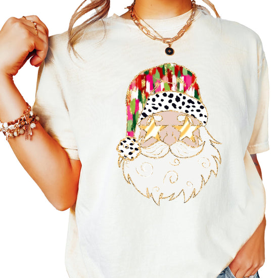 Women's ivory Christmas tee featuring a humorous painted Santa wearing gold sunglasses holiday graphic shirt