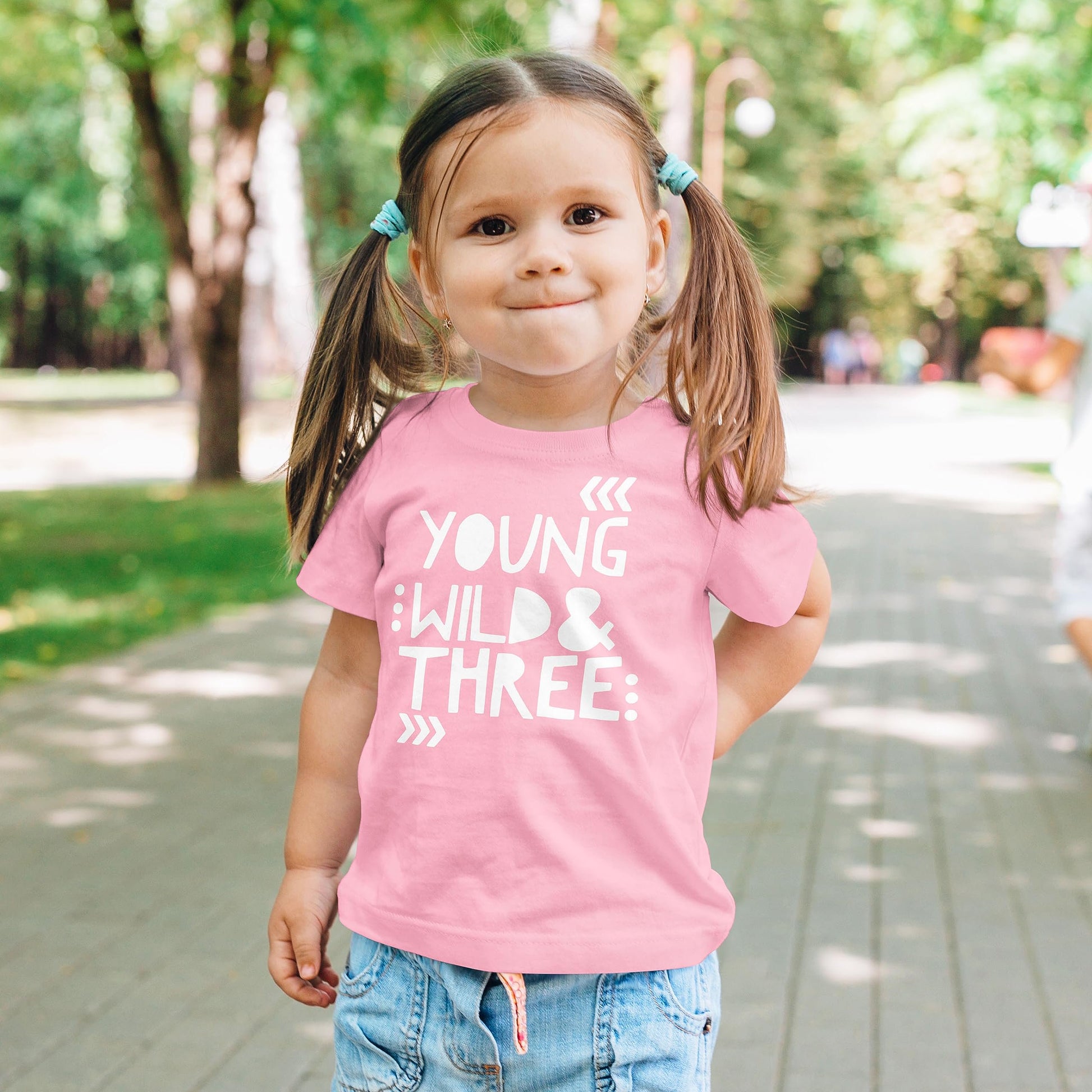 Flat lay of Young Wild and Three girls birthday shirt on peach background