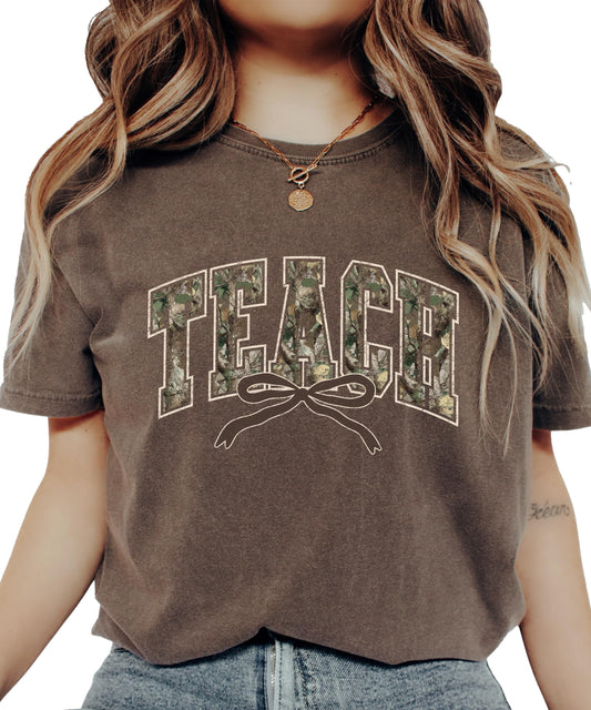 Seafoam green teacher t-shirt with TEACH in camo varsity letters and pink coquette bow detail