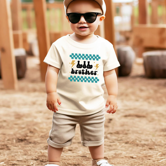 Toddler boy wearing little brother retro lightning graphic shirt in natural color