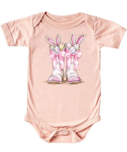Front view of white baby one-piece with western Easter bunny boots graphic in pink and peach
