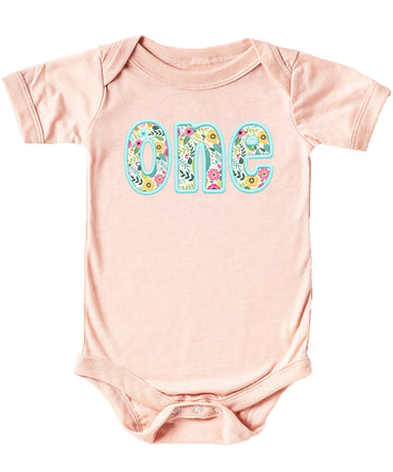 Peach baby girl bodysuit with teal ink-printed floral embroidery celebrating first birthday milestone