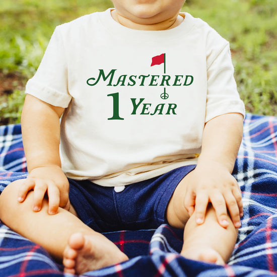 Toddler wearing Mastered 1 Year golf first birthday tee in natural color