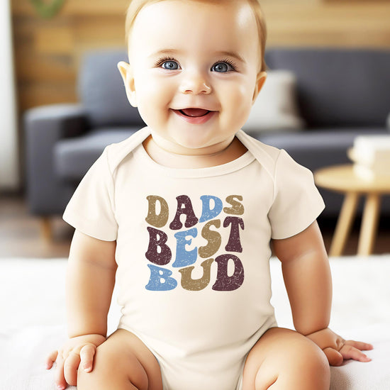 Flat lay of Dad's Best Bud baby bodysuit with retro font design for boys