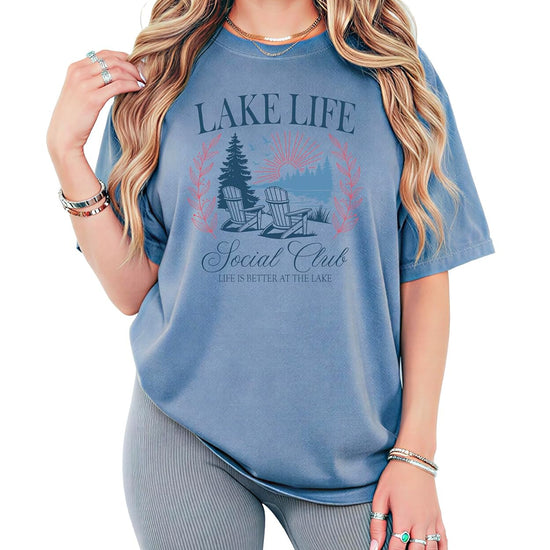 Lake Life Social Club ivory graphic tee with vintage lakeside scene featuring Adirondack chairs and pine trees
