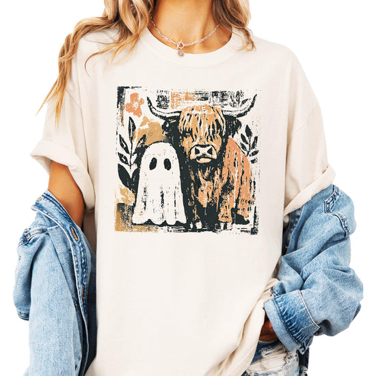 Close-up of ghost and highland cow Halloween graphic print on women's ivory tee shirt