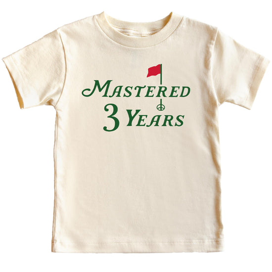 Flat lay of natural toddler birthday tee featuring golf theme and Mastered 3 Years text