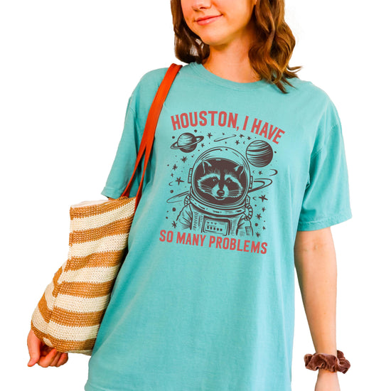 Close-up of astronaut raccoon graphic print with humorous space-themed text on seafoam shirt