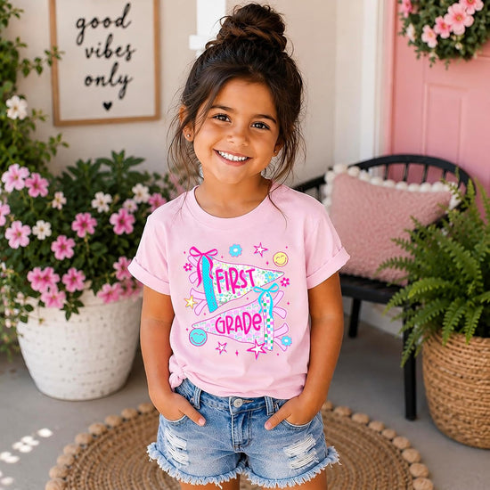 Flat lay of girls 1st grade shirt showing full floral pennant flag graphic in Natural color