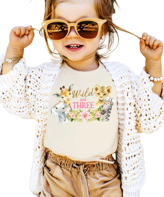 Wild and Three birthday tee displaying giraffe, lion cub, elephant and zebra graphics in vibrant colors