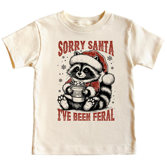 Sorry Santa I've Been Feral natural graphic tee featuring a raccoon in a Santa hat holding hot cocoa