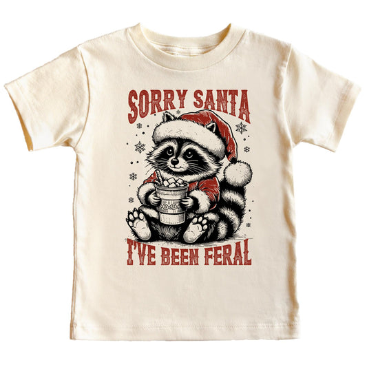 Sorry Santa I've Been Feral natural graphic tee featuring a raccoon in a Santa hat holding hot cocoa