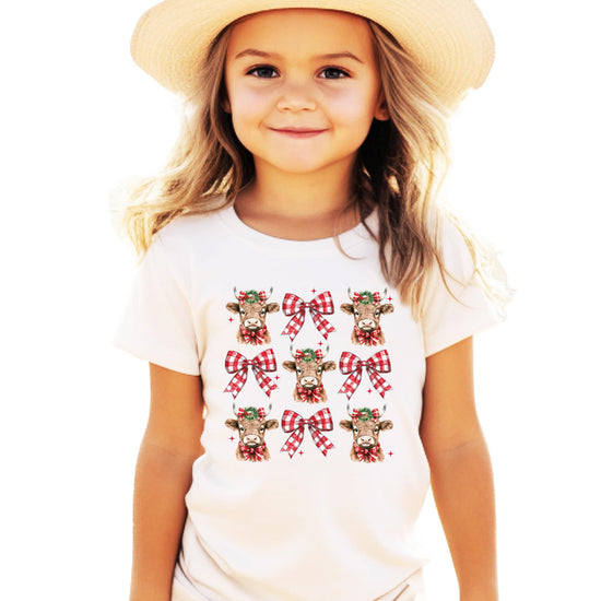 Flat lay of women's festive winter graphic tee with Christmas cow and plaid bow design