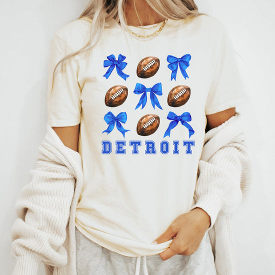 Detail shot of vibrant blue coquette bows and football graphic on women's Detroit shirt