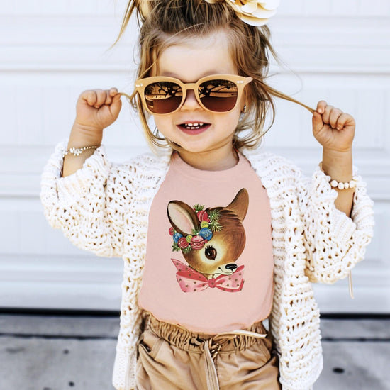 Flat lay of Olive Loves Apple toddler reindeer wreath Christmas tee in peach color