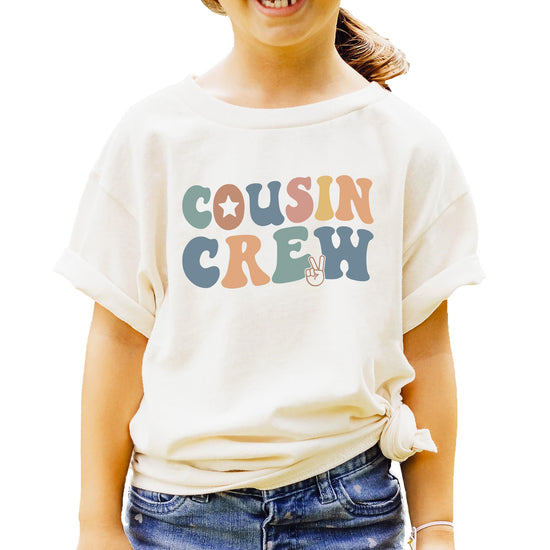 Close-up view of vibrant rainbow colored Cousin Crew lettering on natural tee