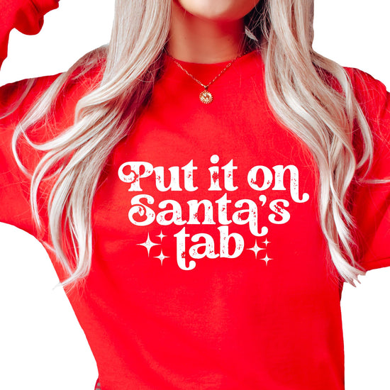 Woman wearing a red 'Put It on Santa's Tab' funny Christmas pullover sweatshirt with bold holiday graphic print