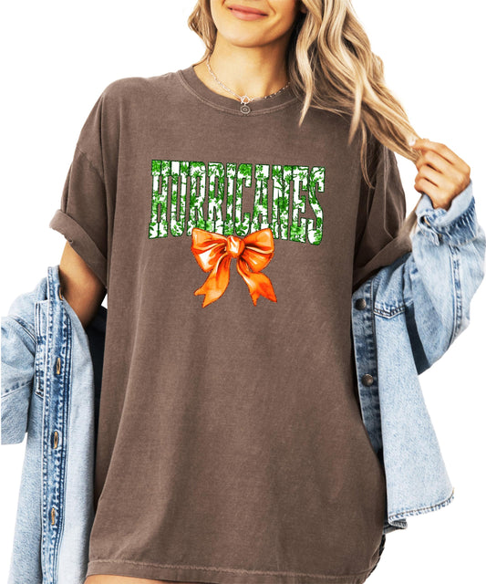 Women's ivory graphic tee with 'Hurricanes' in green floral letters and orange bow accent for school spirit