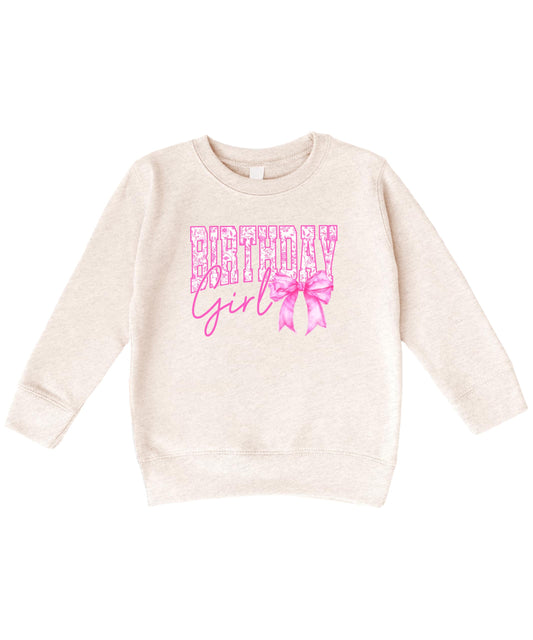Close-up of Birthday Girl bow sweatshirt showing sparkly pink lettering and bow graphic detail