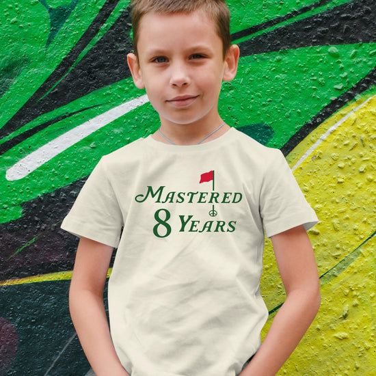 Boys and girls golf themed 8th birthday t-shirt in natural color laid flat