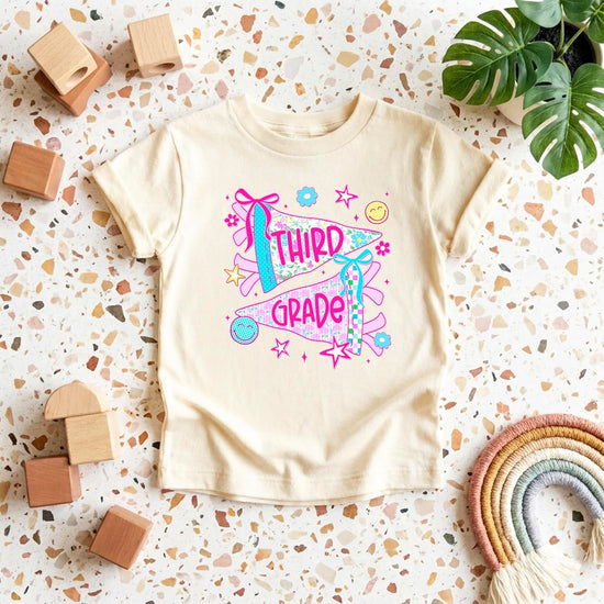 Natural colored kids third grade shirt with hand-drawn pennant flags and coquette bow accents
