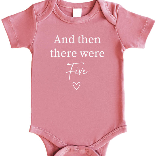 Close-up of And Then There Were 4 heart graphic on mauve baby bodysuit for sibling reveal