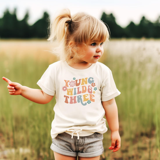 Toddler girl wearing Young Wild Three groovy birthday shirt front view