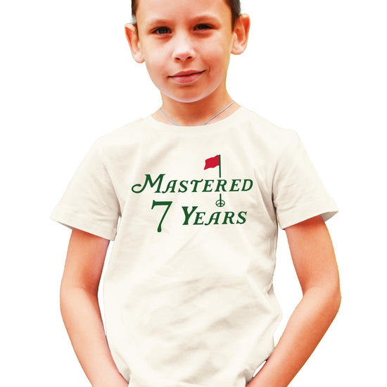 Golf themed seventh birthday shirt for kids laid flat on natural background