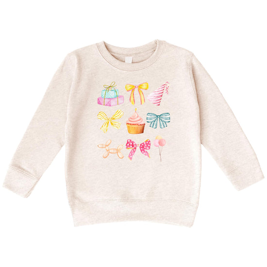 Close-up of pastel coquette birthday graphic on kids sweatshirt featuring bows, cupcakes, and balloons