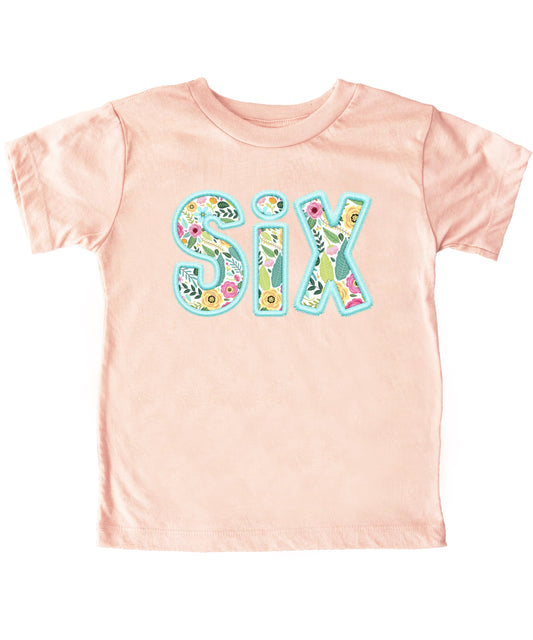 Close-up of teal floral embroidered Six design on peach youth birthday shirt