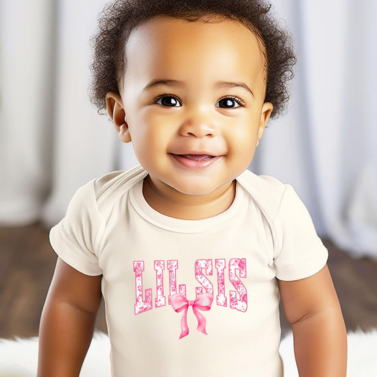 Baby girl wearing Lil Sis natural bodysuit with pink bow floral graphic, newborn outfit