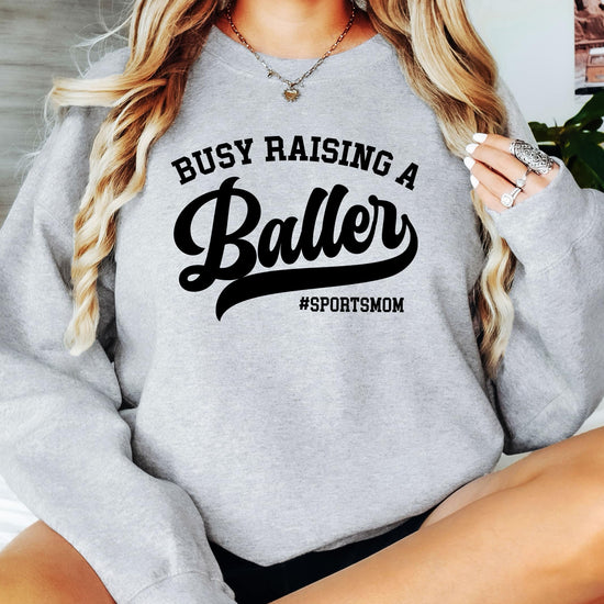 Lifestyle flat lay of women's black sports mom sweatshirt with baller graphic design