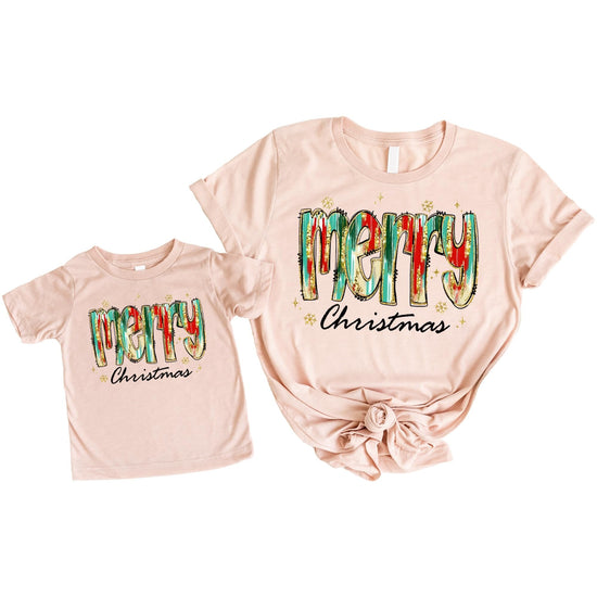 Adult and child wearing matching watercolor Christmas graphic tees in peach