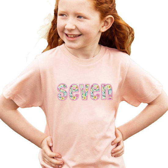 Side view of peach birthday tee with floral seven embroidery detail