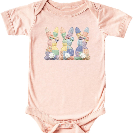 Natural baby bodysuit with three quilt-style bunnies printed in soft spring colors for Easter
